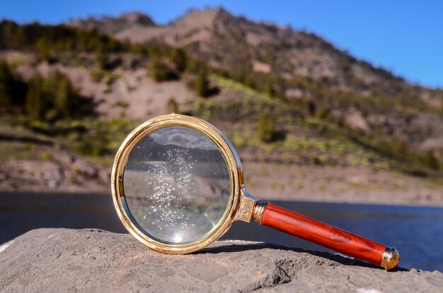 Lupa de vidro da lupa do conceito da investigação na rocha vulcânica perto de um lago