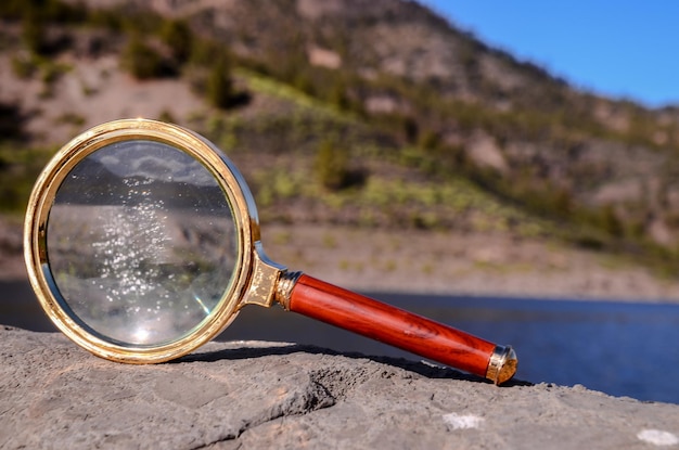 Lupa de vidro da lupa do conceito da investigação na rocha vulcânica perto de um lago