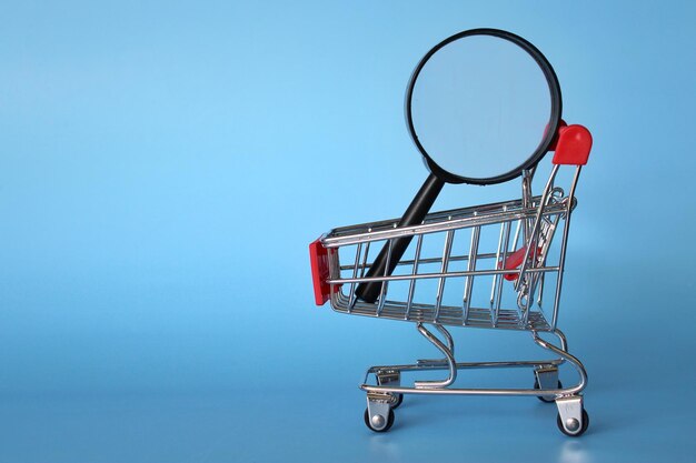 Lupa dentro del carrito de compras Fondo azul Búsqueda de productos y concepto de compras frugales