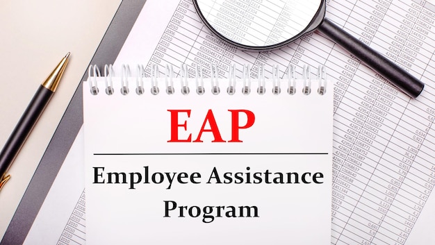 Lupa de escritorio, informes, bolígrafo y cuaderno con texto Programa de asistencia al empleado EAP