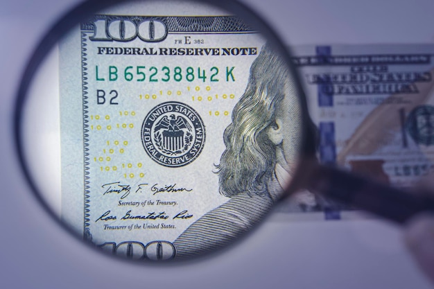 Lupa en el fondo de un concepto de primer plano de 100 dólares sobre el tema de verificar la autenticidad del dinero