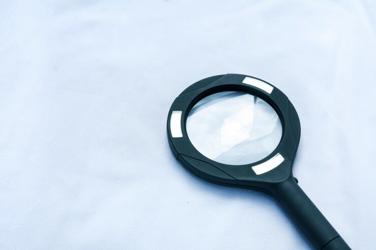 Una lupa negra aislada sobre fondo blanco, con un tono azul que representa la ciencia y la investigación.