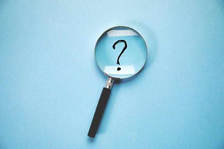 Foto lupa y un signo de interrogación sobre fondo azul.