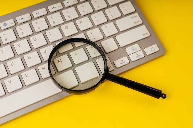 Foto lupa en un teclado sobre un fondo amarillo concepto de búsqueda en internet