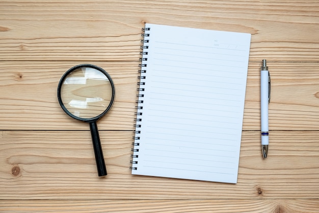 Lupa de vidrio y cuaderno en blanco con lápiz sobre fondo de madera