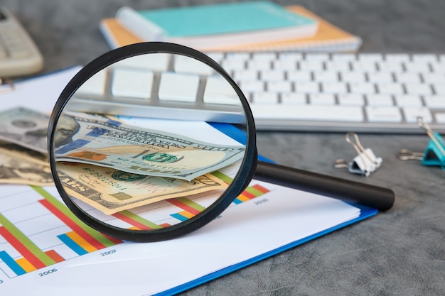 Foto lupe und büromaterial, geld, dokumente, tastatur auf grauem hintergrund.