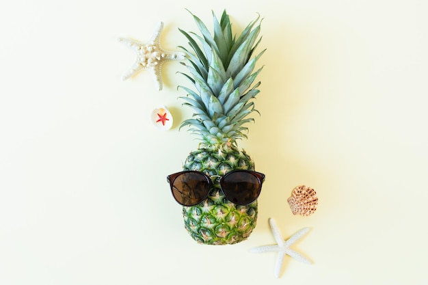 Lustige Ananas mit Sonnenbrille und Muschel auf gelbem Pastellhintergrund Sommerhintergrund