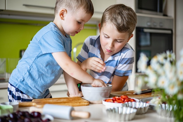 Lustige bruder männliche kinder freuen sich, spaß beim kochen von sommerdessert mit früchten und beeren zu haben