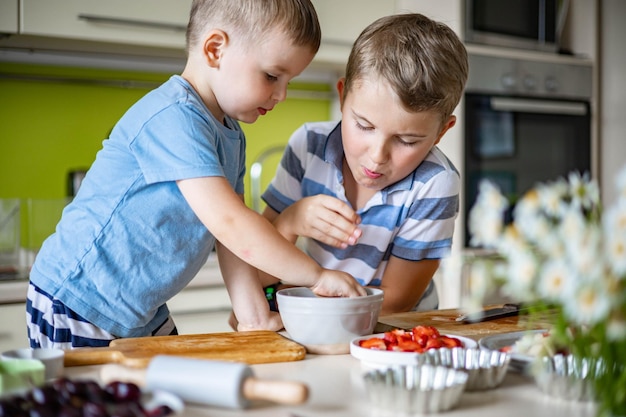 Lustige Bruder männliche Kinder freuen sich, Spaß beim Kochen von Sommerdessert mit Früchten und Beeren zu haben