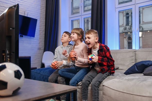 Lustige drei Kinderfreunde sitzen zu Hause auf der Couch und genießen Fußballspiel