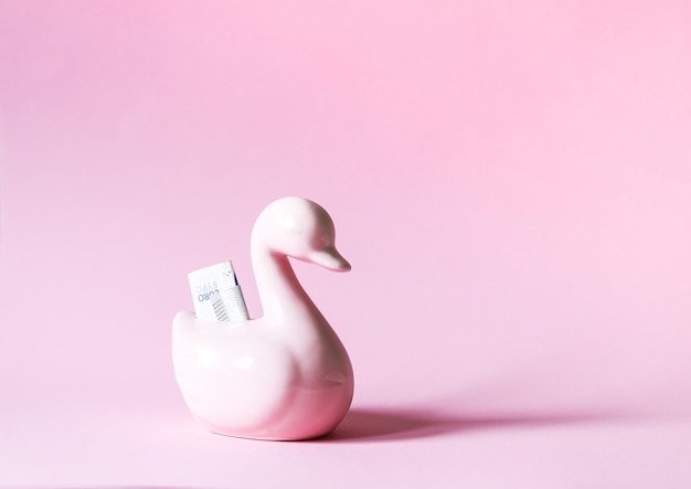 Lustige Ente Sparschwein oder Spardose mit Papiergeld auf weichem Pastellhintergrund.