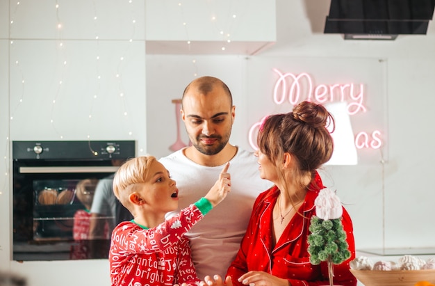 Lustige Familie im Weihnachtspyjama in der Küche, die Kekse macht