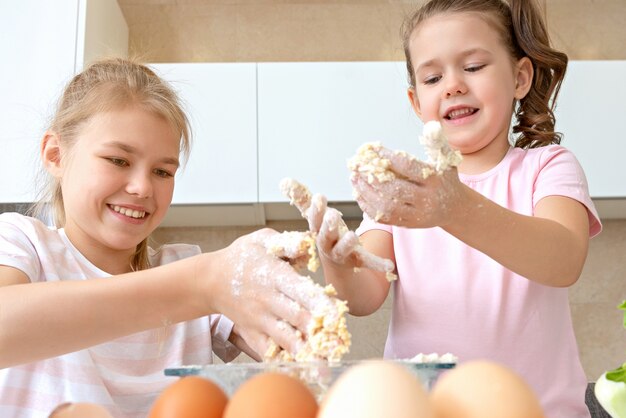 Lustige Familienkinder bereiten den Teig vor, backen Kekse in der Küche. Schwestern haben Spaß zusammen zu lachen