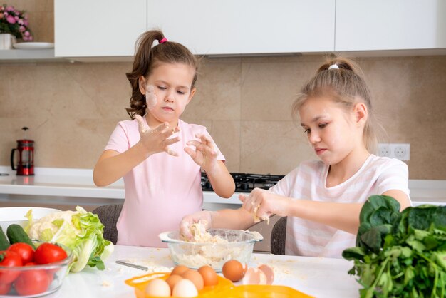 Lustige Familienkinder bereiten den Teig vor, backen Kekse in der Küche. Schwestern haben Spaß zusammen zu lachen