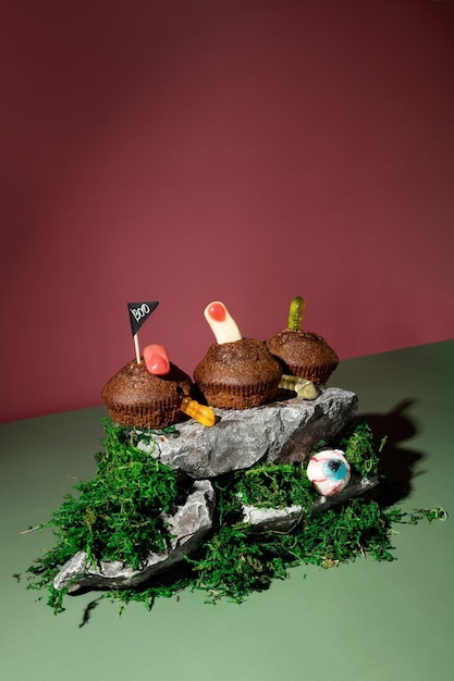 Lustige Halloween-Landschaft. Schreckliche Drohungen. Cupcakes mit Geleewürmern und Fingern steht auf Steinen und Moos