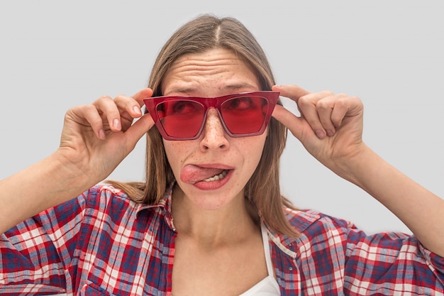 Lustige junge Frau steht nah und schaut durch rote Sonnenbrille nach links.