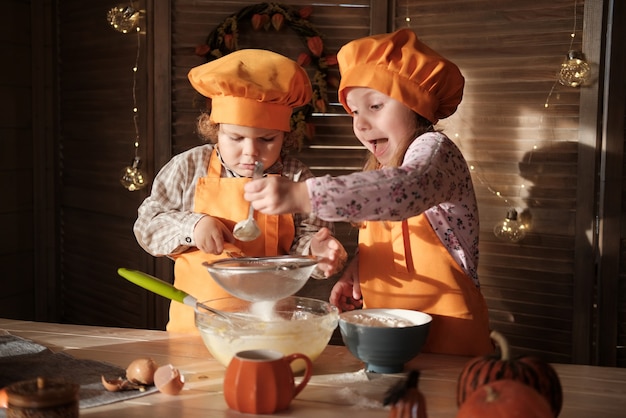 Lustige Jungen und Mädchen in orangefarbenen Kochkostümen bereiten Kürbiskuchen vor. Kinder bereiten sich auf Thanksgiving vor. das Konzept eines Familienurlaubs