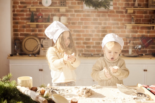 Lustige Kinder der glücklichen Familie bereiten den Teig zu und spielen mit Mehl in der Küche