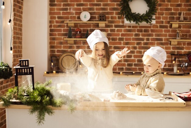 Lustige Kinder der glücklichen Familie bereiten den Teig zu und spielen mit Mehl in der Küche