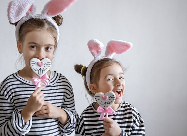 Lustige kleine Mädchen mit Osterohren auf ihren Köpfen und Osterlebkuchen auf Stöcken