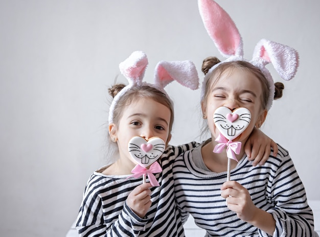 Lustige kleine Mädchen mit Osterohren auf ihren Köpfen und Osterlebkuchen auf Stöcken