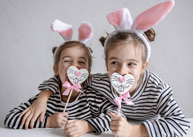 Lustige kleine Schwestern mit Osterlebkuchen in Form von Hasengesichtern und mit Hasenohren