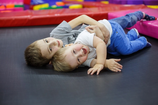 lustige lächelnde Kinder auf Trampolin. älterer Bruder umarmt den jüngeren. aktive Erholung im Kinderzentrum. Jungen spielen im Spielzimmer. kleine Freunde haben Spaß im Spielzimmer. Freundschaft zweier Brüder