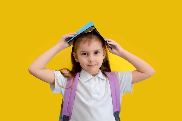 Lustige lächelnde Schulmädchen hält ein Buch auf dem Kopf auf gelbem Hintergrund