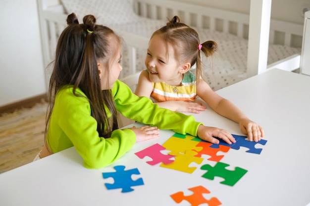 Lustige Mädchen sammeln gemeinsam Rätsel am Tisch im Kinderzimmer