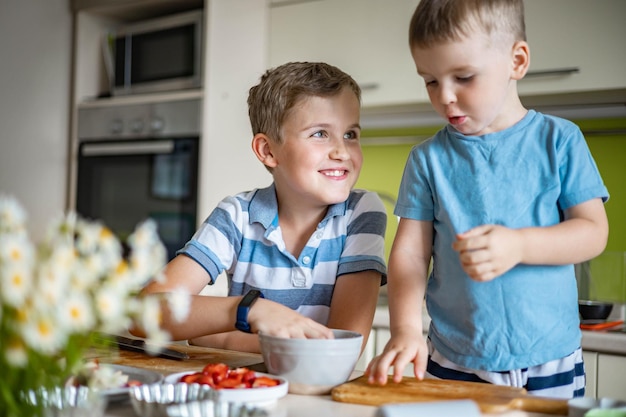 Lustige männliche Kinder des Bruders, die sich freuen, Sommerdessert mit Früchten und Beeren zu kochen