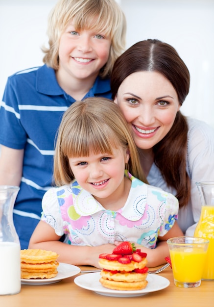 Lustige Mutter und ihre Kinder essen Waffeln mit Erdbeeren