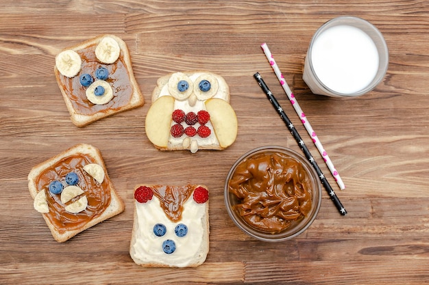 Lustige niedliche Bearmonkeyfoxowl Gesichter Sandwich Toastbrot mit ErdnussbutterBananeHeidelbeereHimbeereMilk Kinder Babys süßes Dessert gesundes Frühstück Mittagessen Essen artclose uptop view