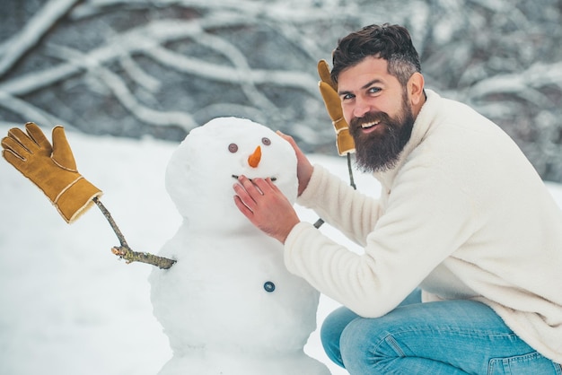 Lustige Schneemänner Glücklicher lächelnder Mann machen Schneemann an einem sonnigen Wintertag Menschen im Schnee Schneemann Handsome Win