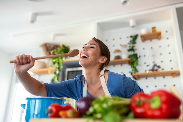 Lustige schöne Frau singt in Pfannenwender, die in der modernen Küche kochen und Pfannenwender als Mikrofontanz halten, Musik hören verspieltes Mädchen, das Spaß mit Küchenutensilien hat, die Essen zubereiten