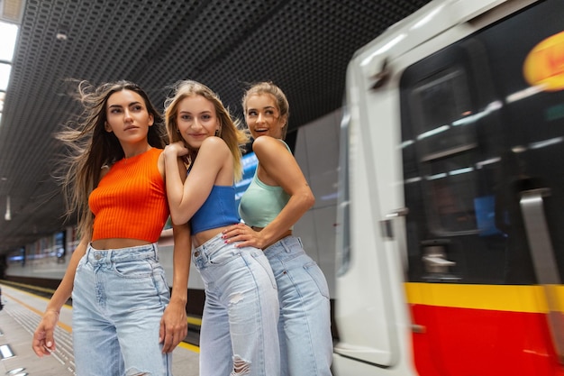 Lustige schöne Freundinnen in modischer Straßenkleidung mit Top und Jeans in der U-Bahn in der Nähe des fahrenden Zuges