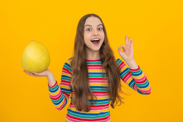 Lustige Teenager-Mädchen halten Zitrusfrüchte Pummelo oder Pampelmuse große grüne Grapefruit isoliert auf gelbem Hintergrund Aufgeregtes Gesicht fröhliche Emotionen von Teenager-Mädchen