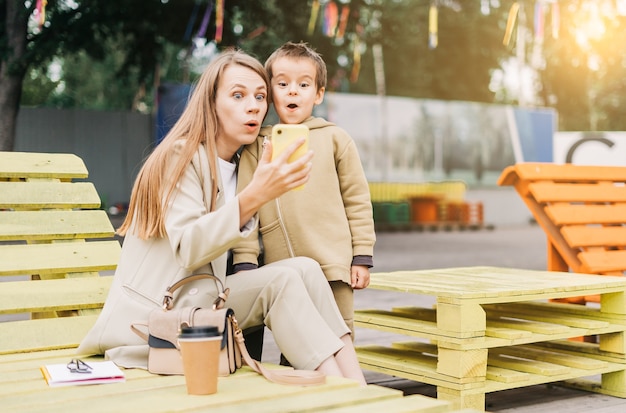 Lustige und überraschte junge Mutter mit Sohn im Vorschulalter sitzen auf Bank