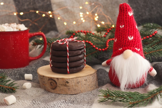 Lustige Weihnachtskarte mit Spielzeug-Gnom-Becher heißer Schokolade mit Marshmallow-Keksen auf Holzschnitt