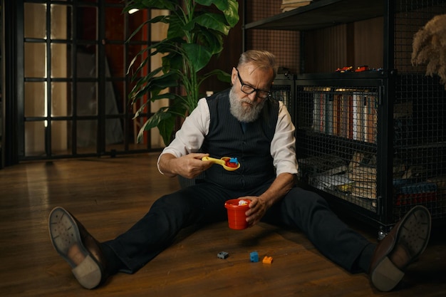 Lustiger älterer Geschäftsmann, der Spielzeug spielt, während er auf dem Boden sitzt
