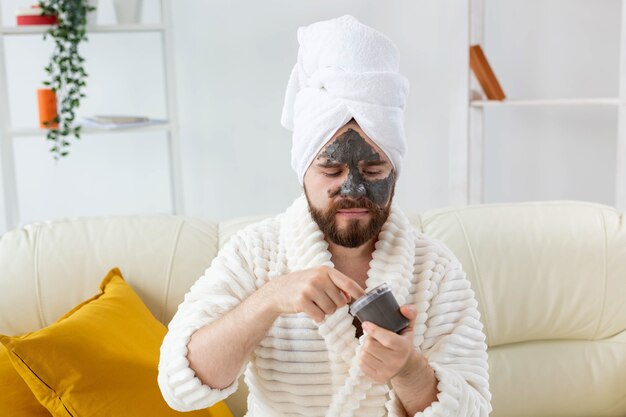 Lustiger bärtiger Mann, der sich mit einer kosmetischen Maske auf seinem Gesicht aus schwarzem Ton amüsiert