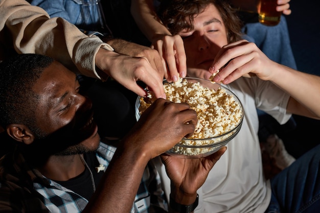 Lustiger Film mit Freunden. Gruppe von Leuten, die Popcorn essen, während sie einen Film im Fernsehen sehen, zu Hause, Popcorn aus der Schüssel nehmen, Wochenenden genießen. Ansicht von oben