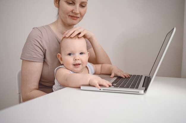 Lustiger Gesichtsausdruck des nahen Porträts des kleinen Jungen, der auf dem Schoß der Mutter sitzt und Laptop studiert