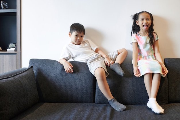 Foto lustiger jugendlicher vietnamesischer bruder und schwester, die auf dem sofa im wohnzimmer sitzen und in die kamera schauen