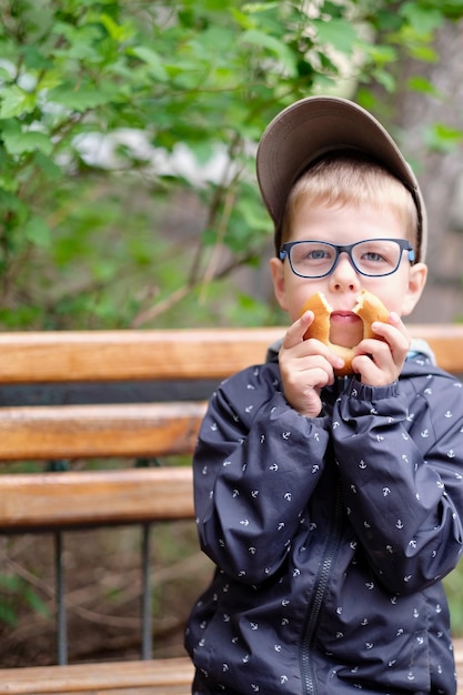 Lustiger Junge mit Brille und Bagel Urkomisches Foto eines Kindes mit Brille Ein Junge mit Sehschwäche Ein Kind posiert und albert für die Kamera herum