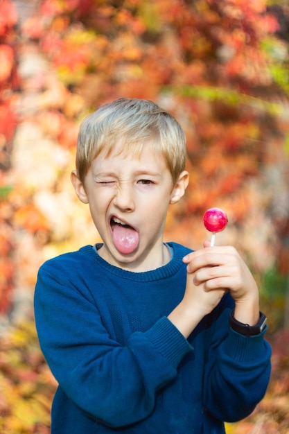 lustiger Junge zeigt seine Zunge vor dem Hintergrund der Herbstbäume