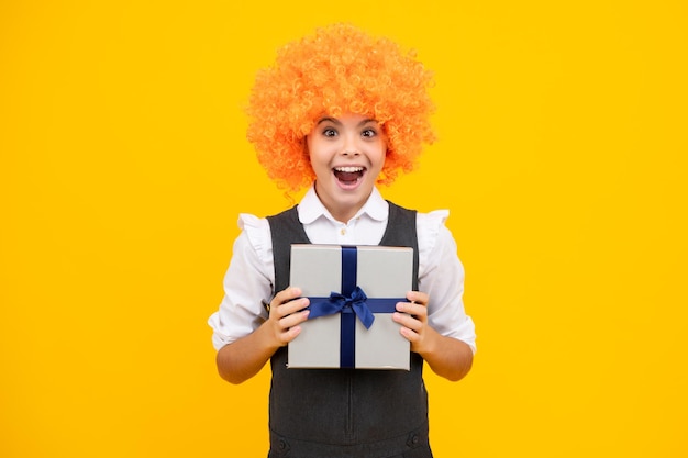 Lustiger Kinderclown in Perücke und Geschenk Kind mit Geschenkbox auf isoliertem Studiohintergrund Gifting für Kindergeburtstag Aufgeregtes Gesicht fröhliche Emotionen von Teenager-Mädchen