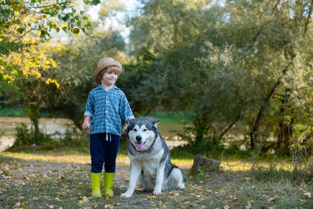 Lustiger Kinderjunge mit Hund geht zusammen auf grünem Feldabenteuer und Ferienkinderkonzeptch ...