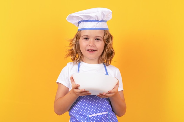 Lustiger Kinderkoch mit Küchenteller, Studioporträt. Kinderkoch, Kochstudioporträt. Kinder kochen. Teenager-Junge mit Schürze und Kochmütze