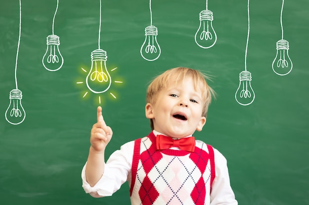 Lustiger Kinderschüler, der Finger gegen grüne Tafel zeigt.