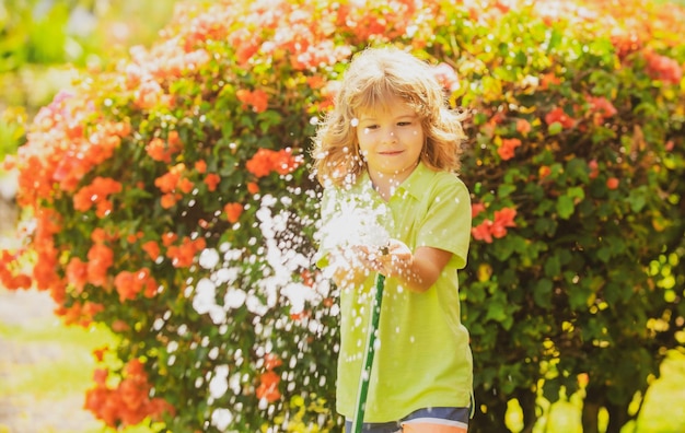 Lustiger kleiner Junge, der mit Gartenschlauch im Hinterhof spielt Kind, das Spaß mit Wasserstrahl hat Sommer ou